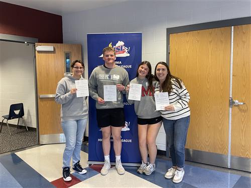 Four people holding certificates stand in front of a Virginia High School League banner.